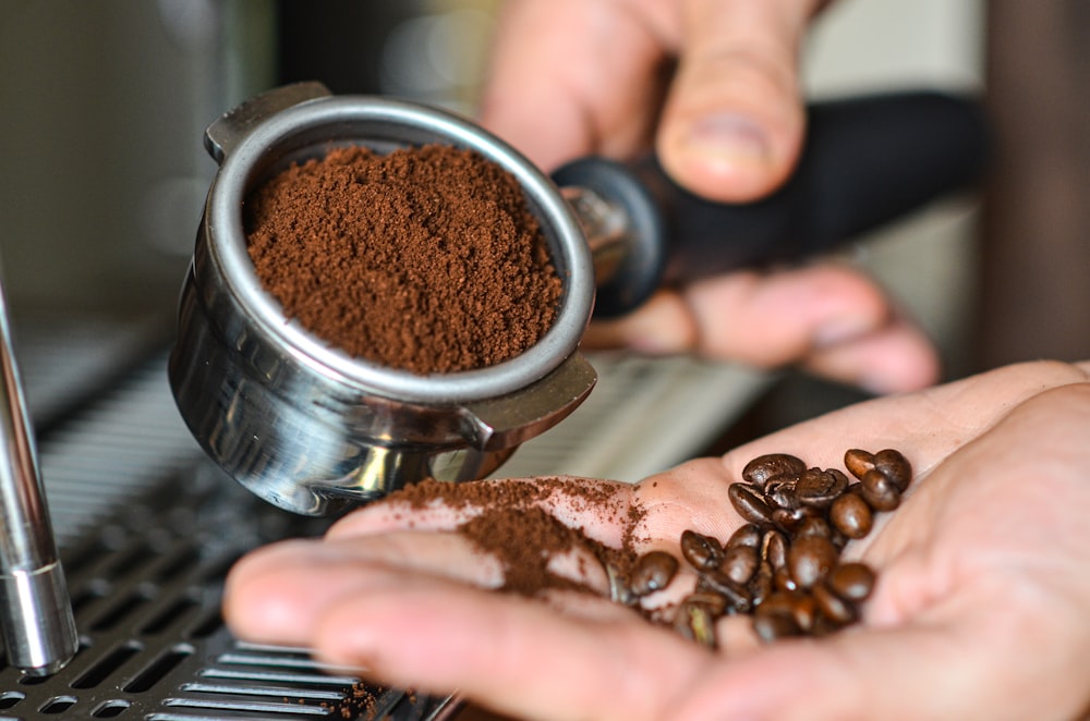 person holding stainless steel cup with coffee beans