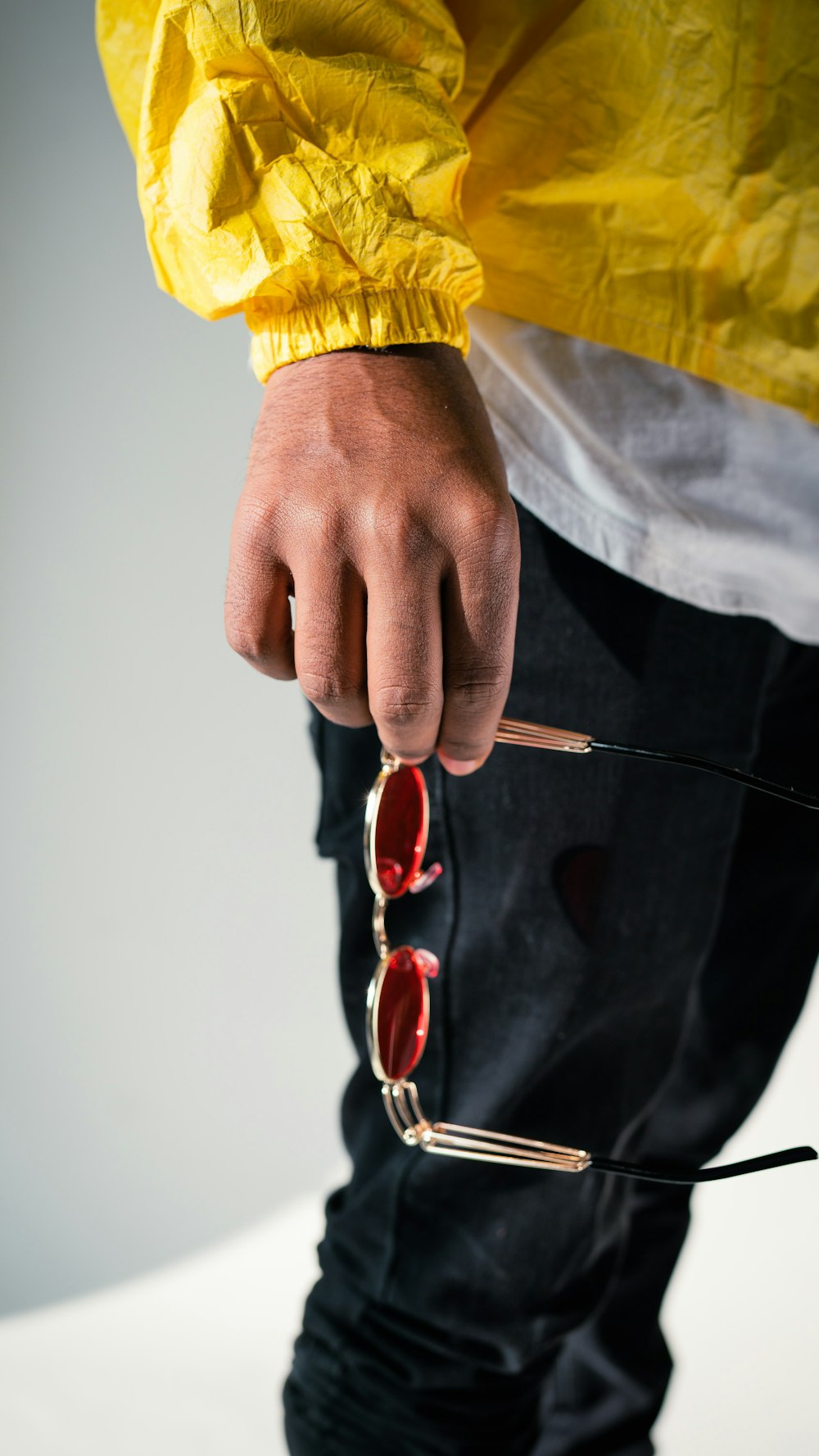 person in black and yellow long sleeve shirt holding red framed sunglasses