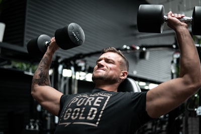 man in black crew neck t-shirt holding black and silver dumbbell determined teams background