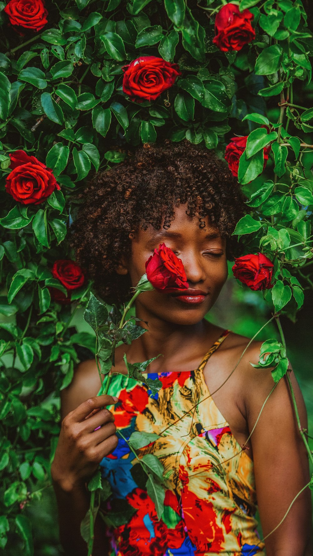 woman in yellow and red floral dress holding red rose