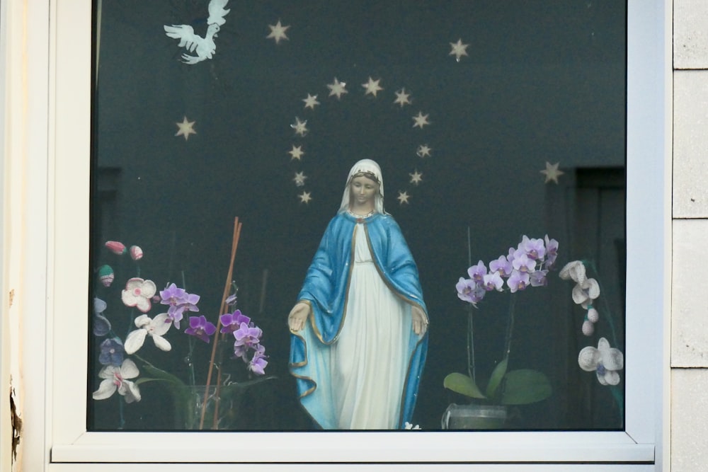 Figura de la Virgen María cerca de las flores moradas