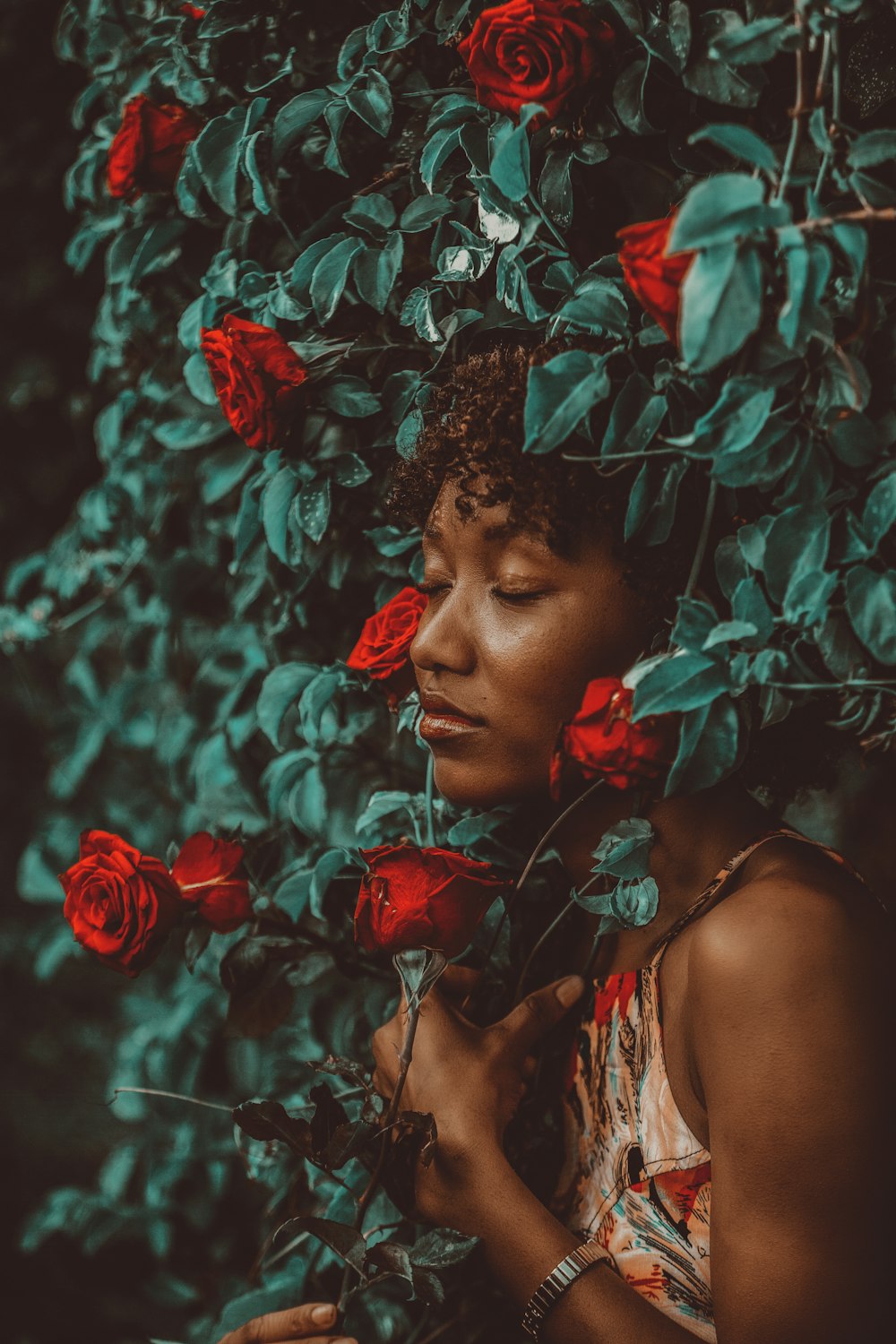 woman in red floral dress standing beside red flowers