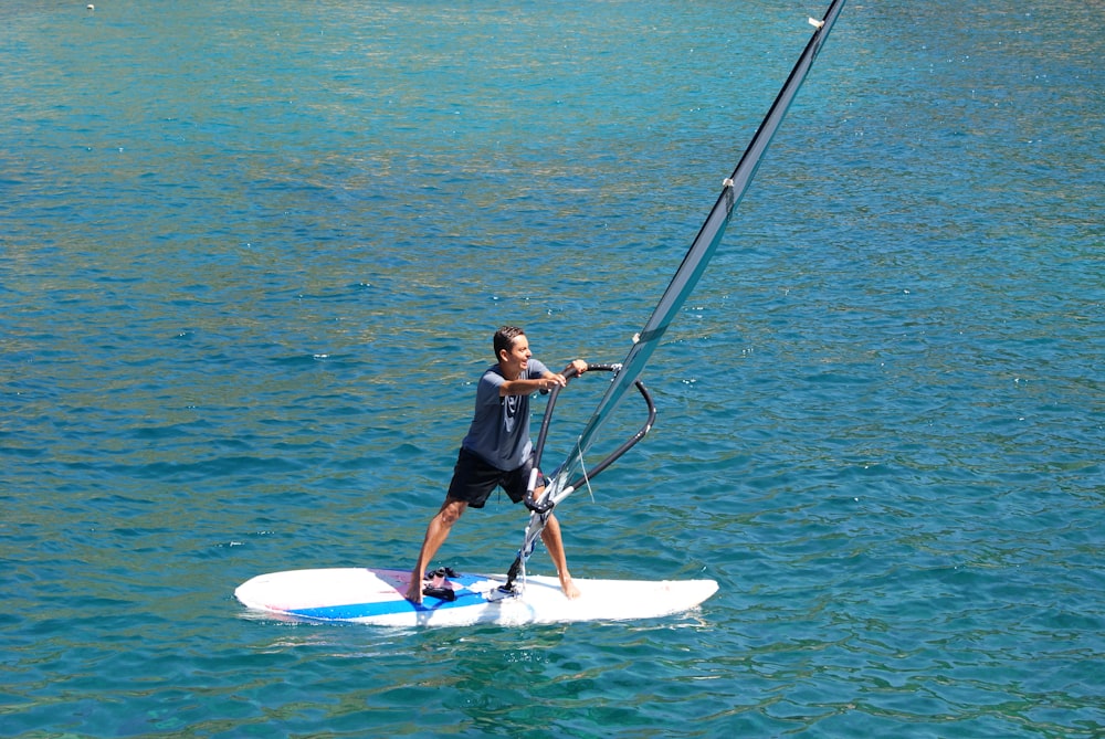 Hombre con camisa negra y pantalones cortos negros montando una tabla de surf blanca en el mar azul durante el día
