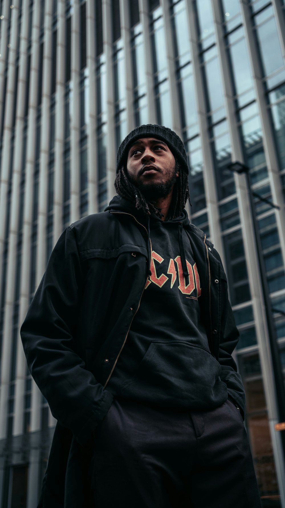 man in black and red hoodie standing near black metal gate during daytime