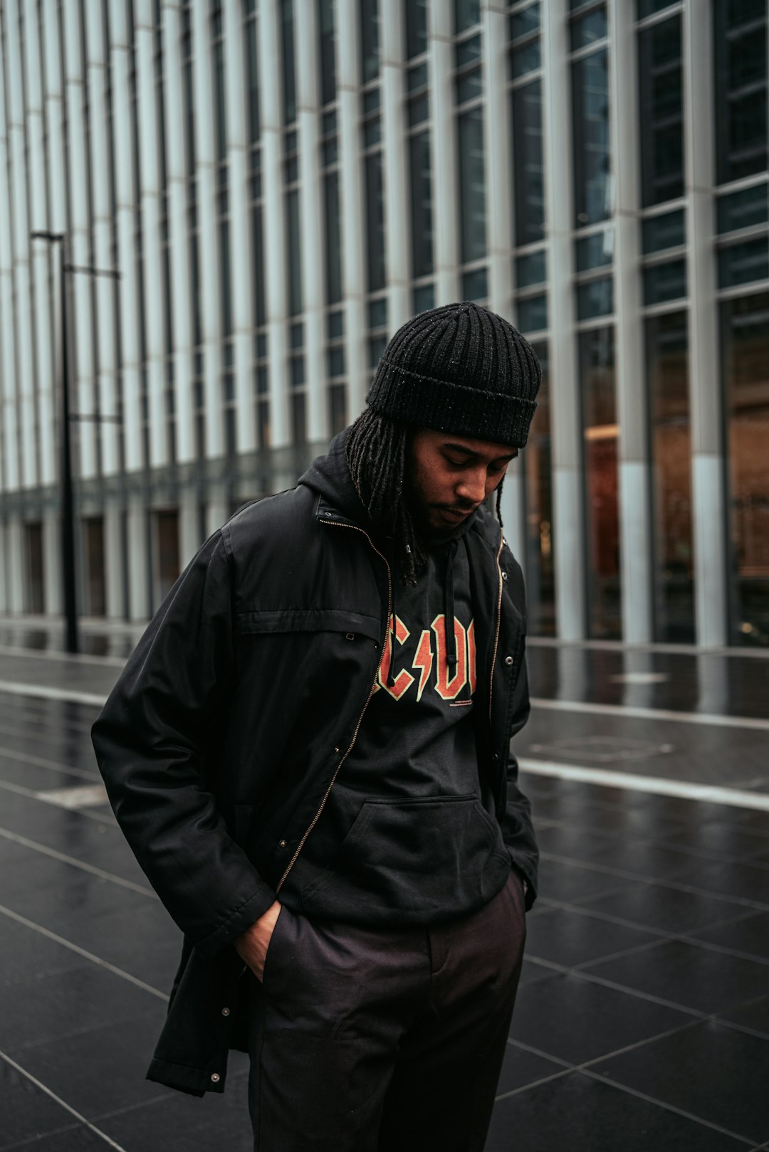 man in black hoodie standing on sidewalk during daytime