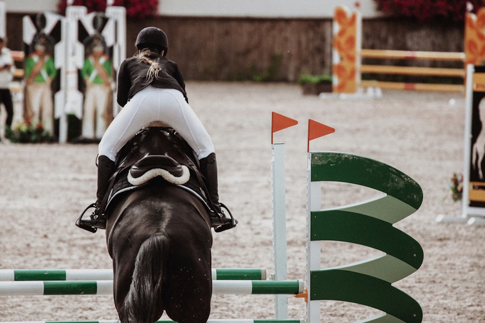 Frau im weißen Hemd reitet tagsüber auf einem schwarzen Pferd