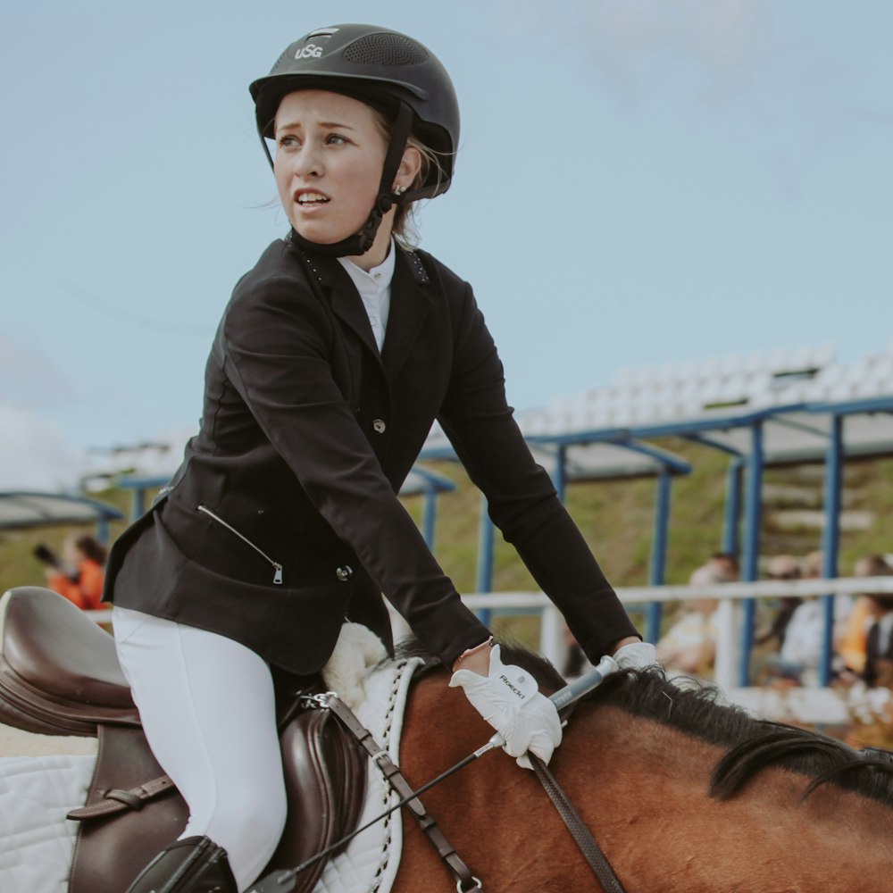 woman in black jacket riding brown horse during daytime