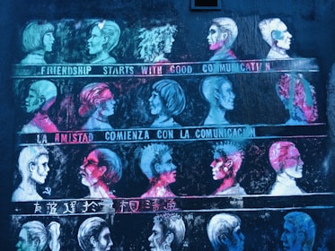 A mural features rows of stylized profile portraits in various vibrant colors. Each row is accompanied by a phrase about communication in different languages, including English, Spanish, and Chinese. The artwork uses contrast between bright neon colors and a dark background to highlight the faces.