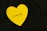 A yellow heart-shaped note with the words 'I LOVE YOU' written in black is placed on a dark background.