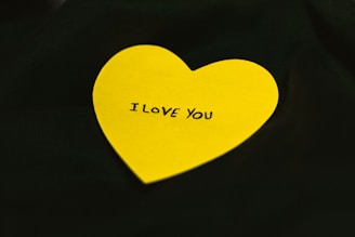 A bright yellow heart-shaped paper with the words 'I LOVE YOU' written on it, placed against a dark background.