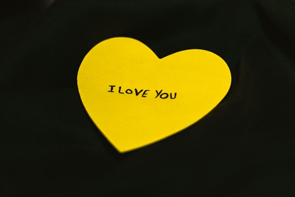 A bright yellow heart-shaped paper with the words 'I LOVE YOU' written on it, placed against a dark background.