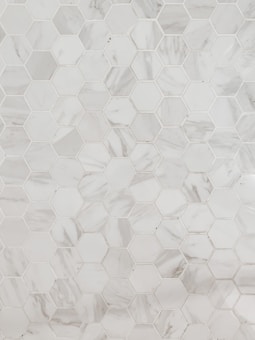 A pattern of hexagonal marble tiles with varying shades of white and grey, creating a geometric and elegant design.