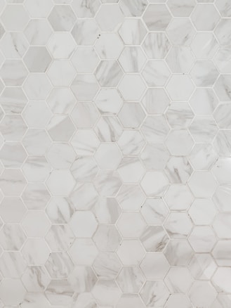A pattern of hexagonal marble tiles with varying shades of white and grey, creating a geometric and elegant design.
