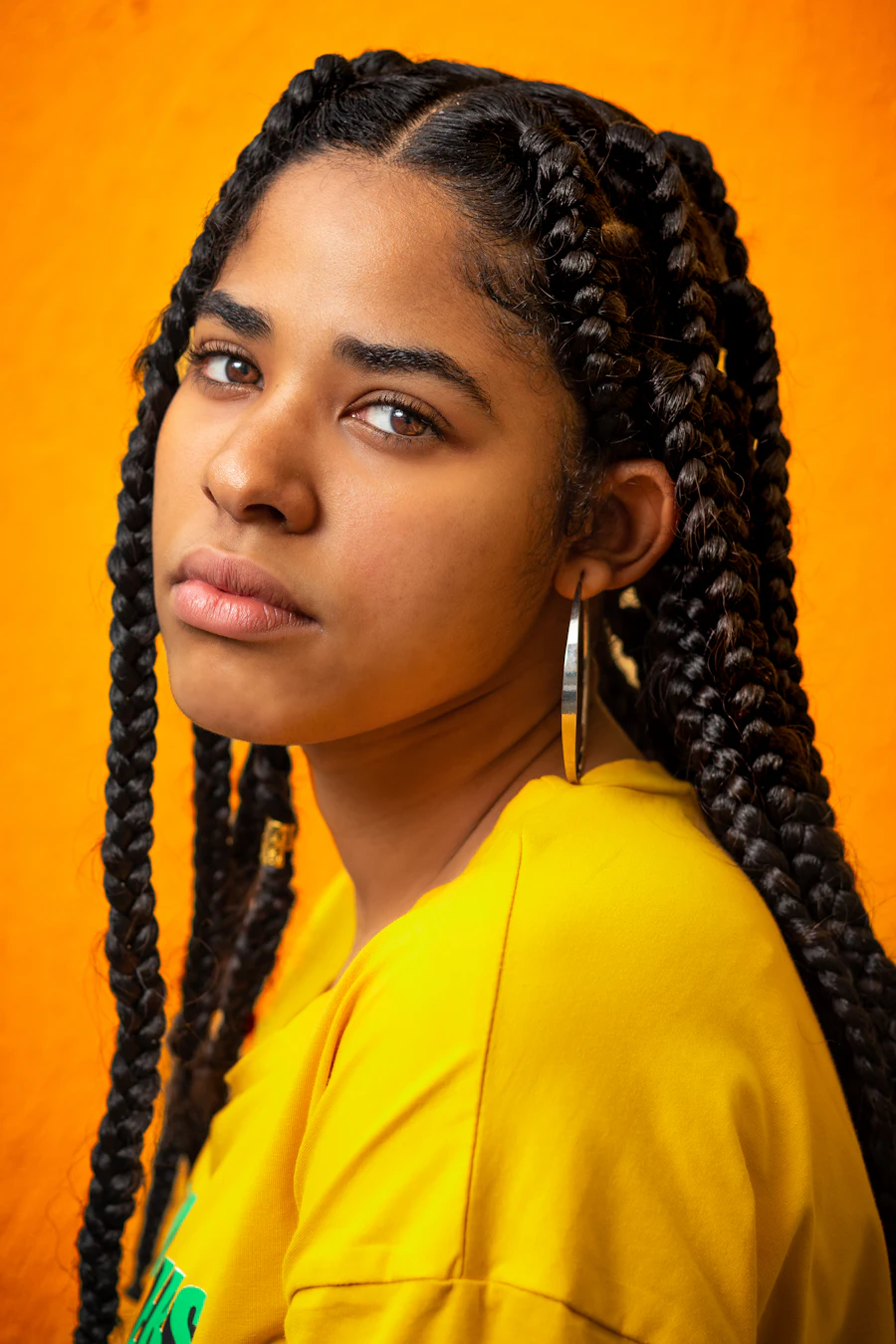 Woman against an orange ground wearing box braids with visible triangle parts