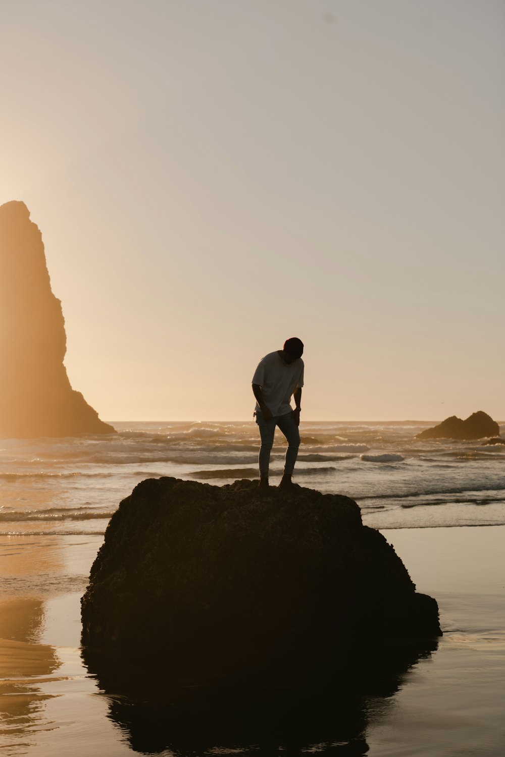 homme en short noir debout sur une formation rocheuse près de la mer pendant la journée