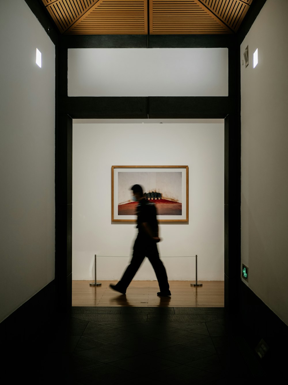 a man walking down a hallway next to a painting
