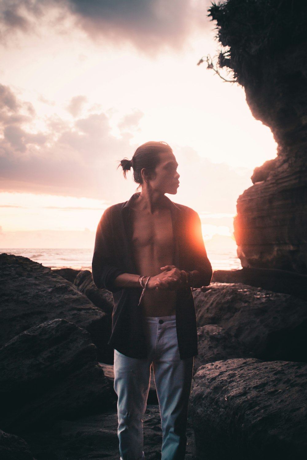 man in blue denim jeans standing on rock formation during sunset
