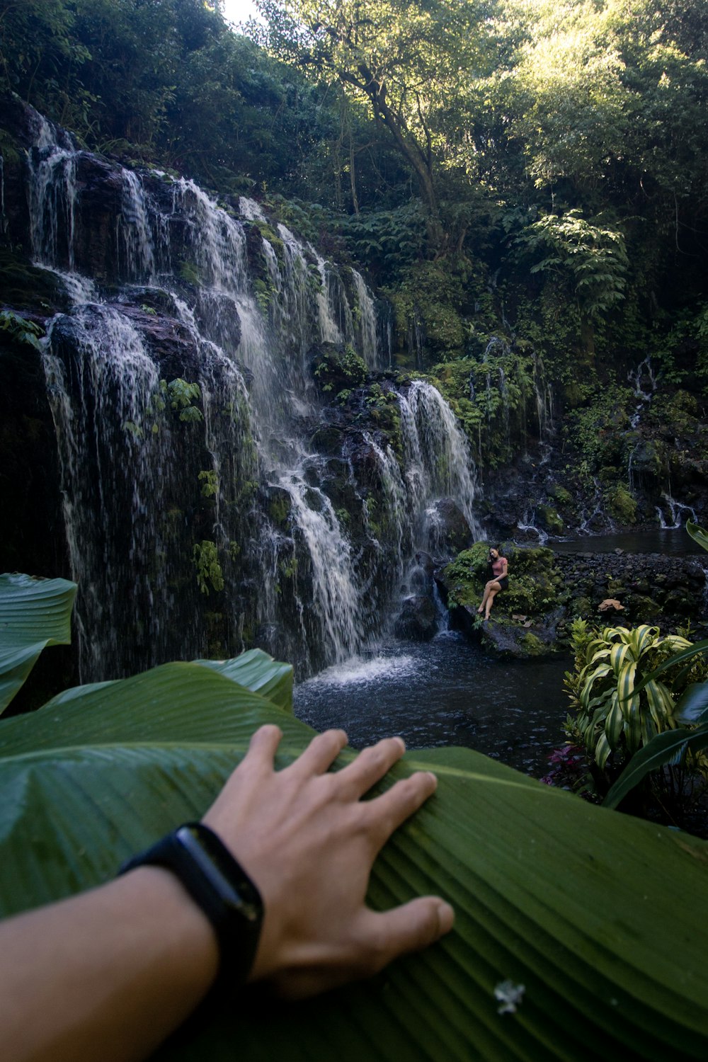 person in green long sleeve shirt sitting on green grass near waterfalls during daytime