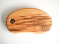 A wooden cutting board with a smooth, rounded shape and a large hole on one end. The wood grain is visible, showing natural brown and beige tones. A brand logo is etched into the bottom right corner with the words 'WOODTOUCH Australia' and an image of a tree.