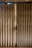 A weathered folding metal gate with vertical slats, exhibiting rust and grime. The gate is situated at the entrance of a structure with beige tiles on the ground. Three round lights are embedded in the ceiling above.