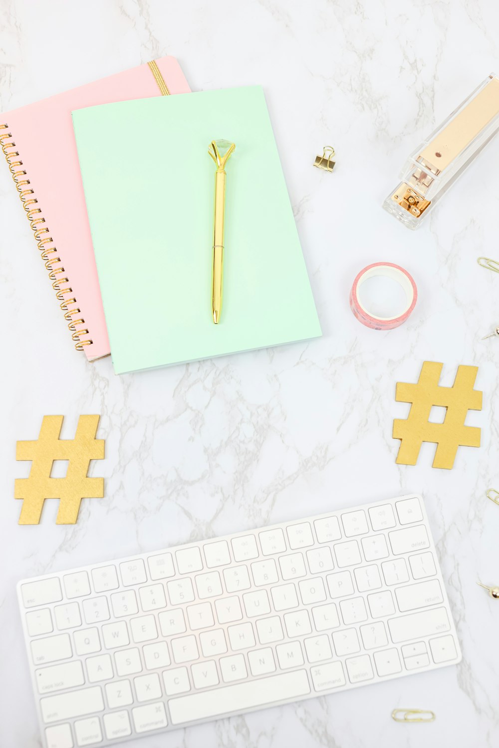 white and gold apple keyboard beside white and gold pen