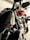 Two motorcycles are parked in an indoor setting. One bike, predominantly black, prominently features the brand name on the fuel tank. The other motorcycle appears to be red. The setting suggests an industrial or garage-like environment with pipes visible in the background.
