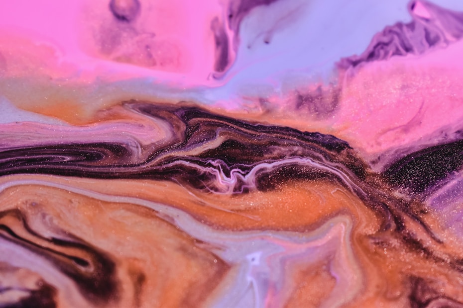 A vibrant swirl of colors, with shades of pink, purple, and orange blending together in a fluid, marbled pattern. The texture appears smooth and flowing, resembling liquid or cream with a glossy finish.