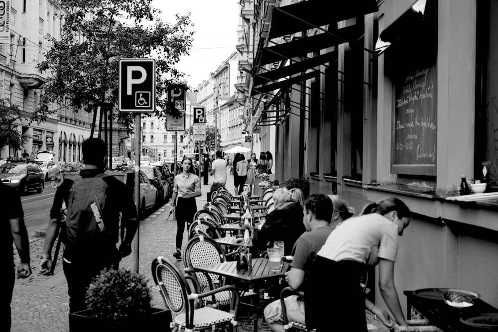 grayscale photo of people sitting on chairs near building