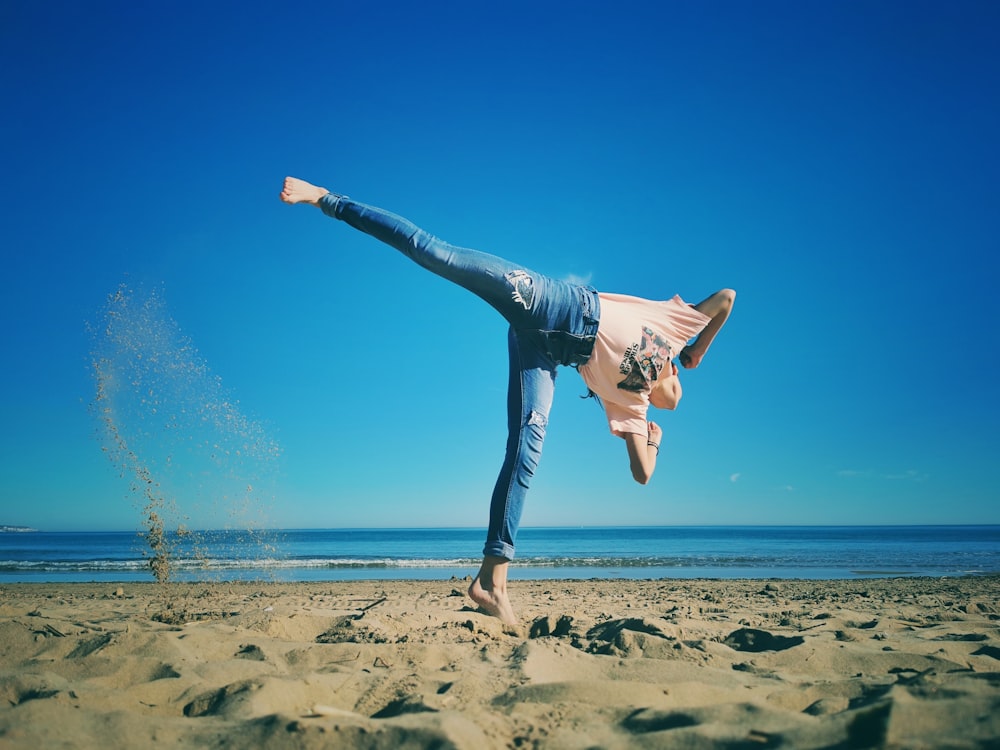 woman in white shirt and blue denim jeans jumping on beach during daytime