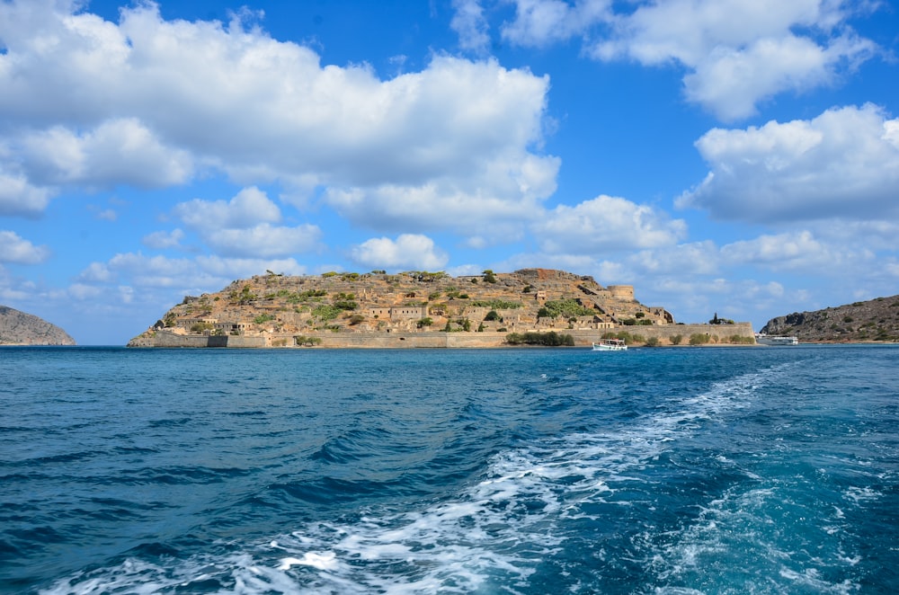 body of water near brown and green mountain under blue and white sunny cloudy sky during