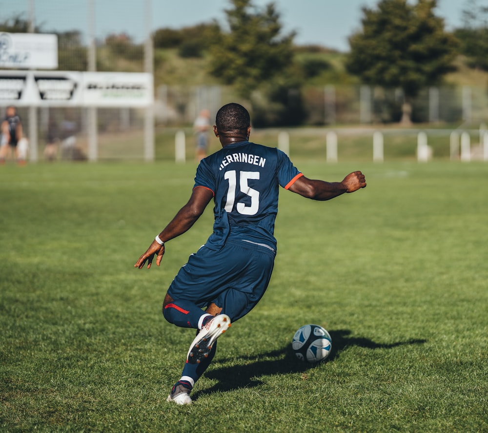 hombre con camiseta azul y blanca jugando al fútbol durante el día