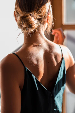 A model wearing a modern, modest dress in soft coffee tones, standing by a sunlit window.