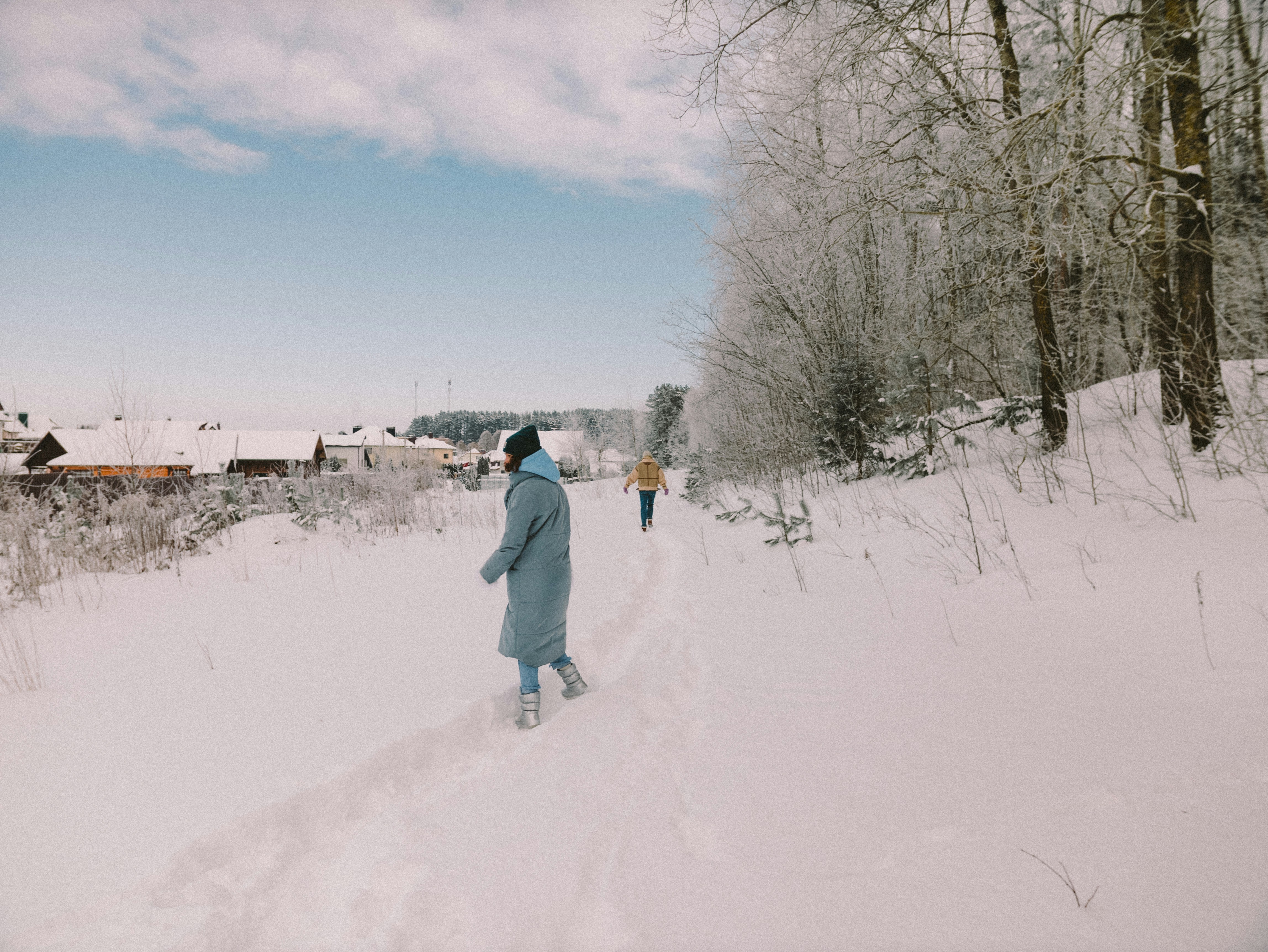 man in white jacket and blue denim jeans walking on snow covered ground during daytime