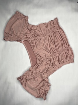 A piece of clothing laid flat on a light-colored surface. The material has a soft, gathered texture and appears to be a one-piece garment with short sleeves.