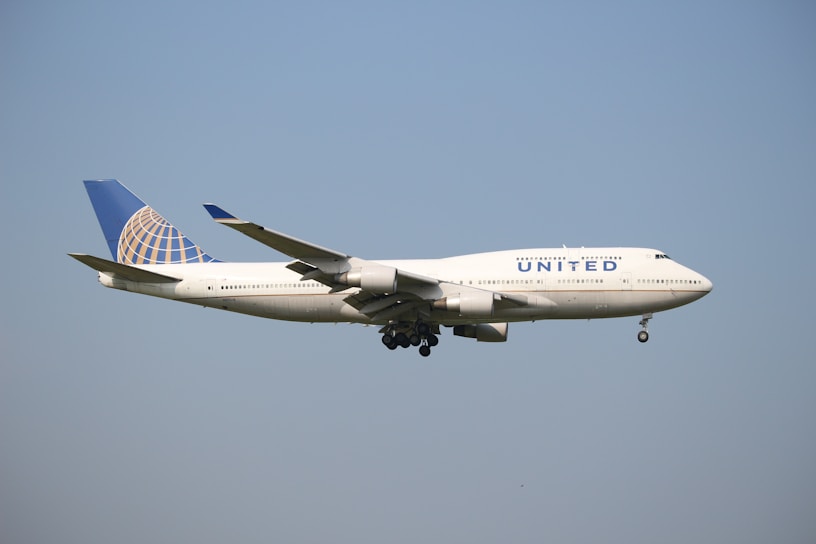 A large passenger airplane with 'United' written on the side is flying against a clear blue sky. The aircraft has a distinctive blue and gold globe logo on its tail.
