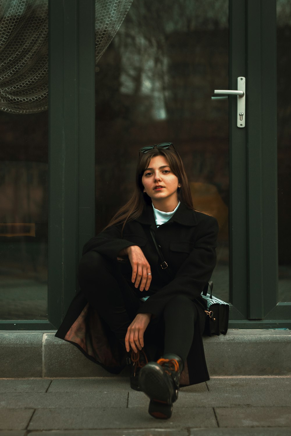 woman in black coat sitting on the sidewalk