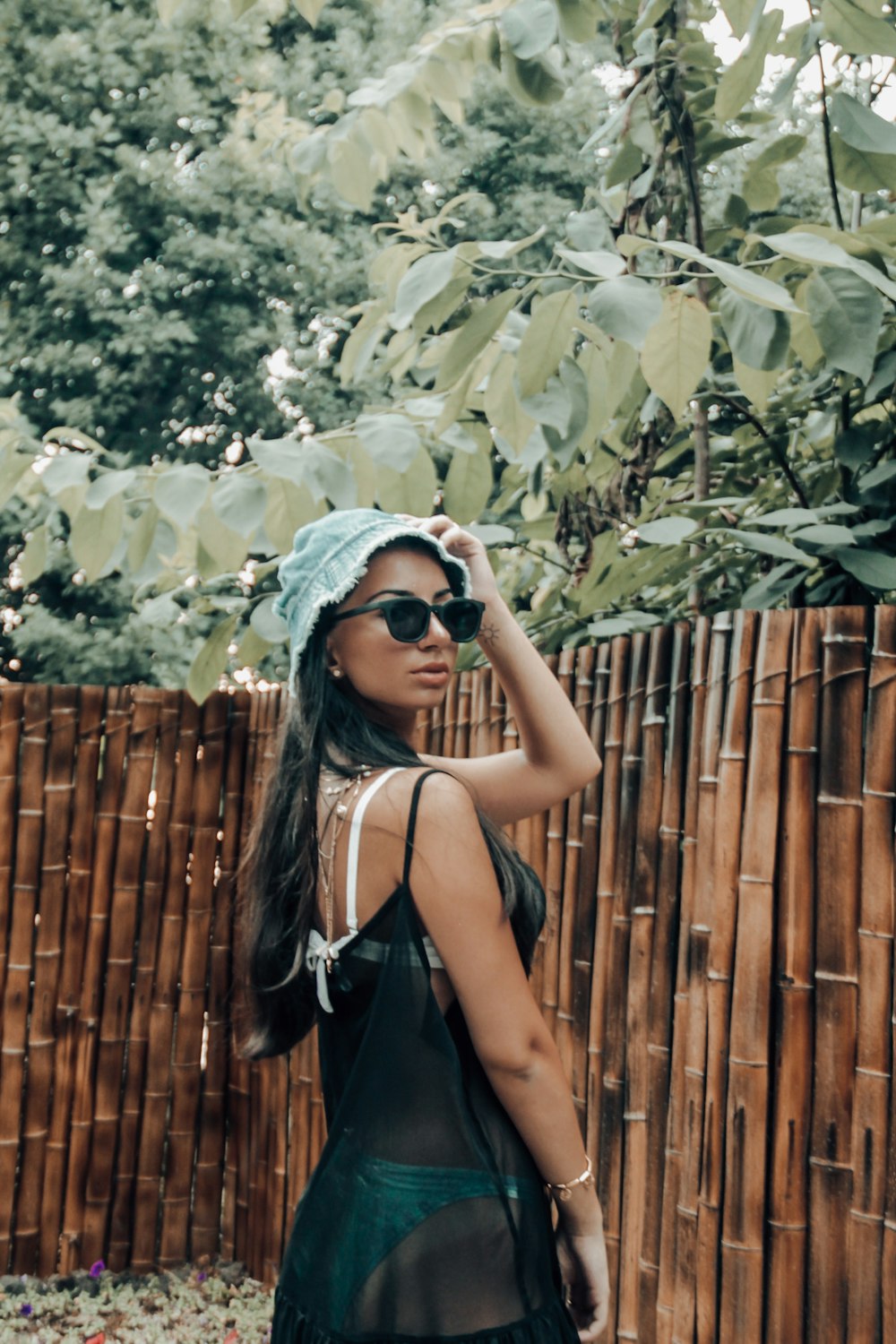 woman in black spaghetti strap top wearing white hijab standing beside brown wooden fence during daytime