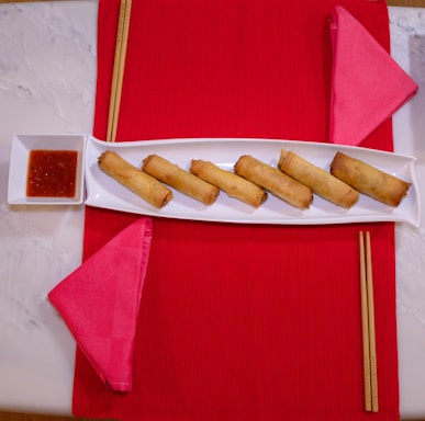 A warm, elegant plate of traditional Chinese spring rolls arranged on a cream-colored ceramic dish with subtle dark red accents.