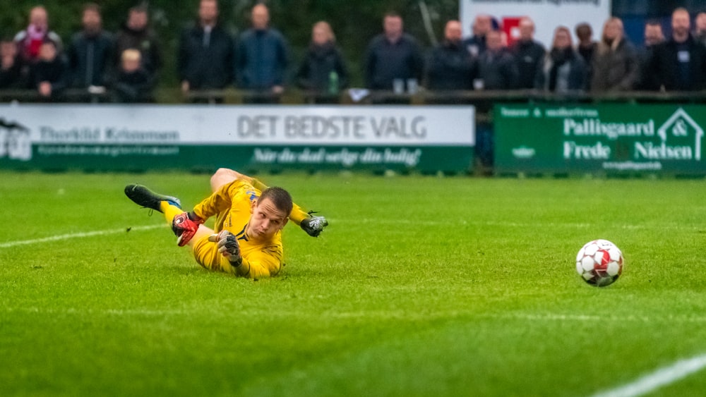 man in yellow jacket playing soccer during daytime