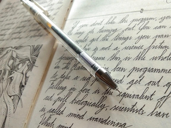 An open journal page with handwritten notes and a golden pen resting on it.