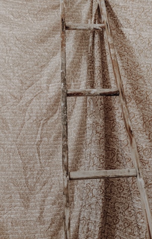 A rustic wooden blanket ladder leaning against a cozy living room wall with soft throws draped over it.