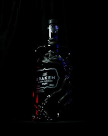 A dark, moody photo of a Kraken Black Spiced Rum bottle. The bottle is intricately designed with tentacle shapes embossed on the glass, highlighted with subtle lighting that emphasizes the mysterious and rich branding.