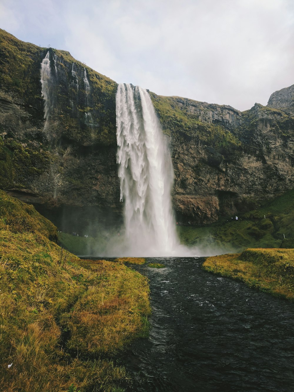 waterfalls on green grass covered hill under white cloudy sky during daytime