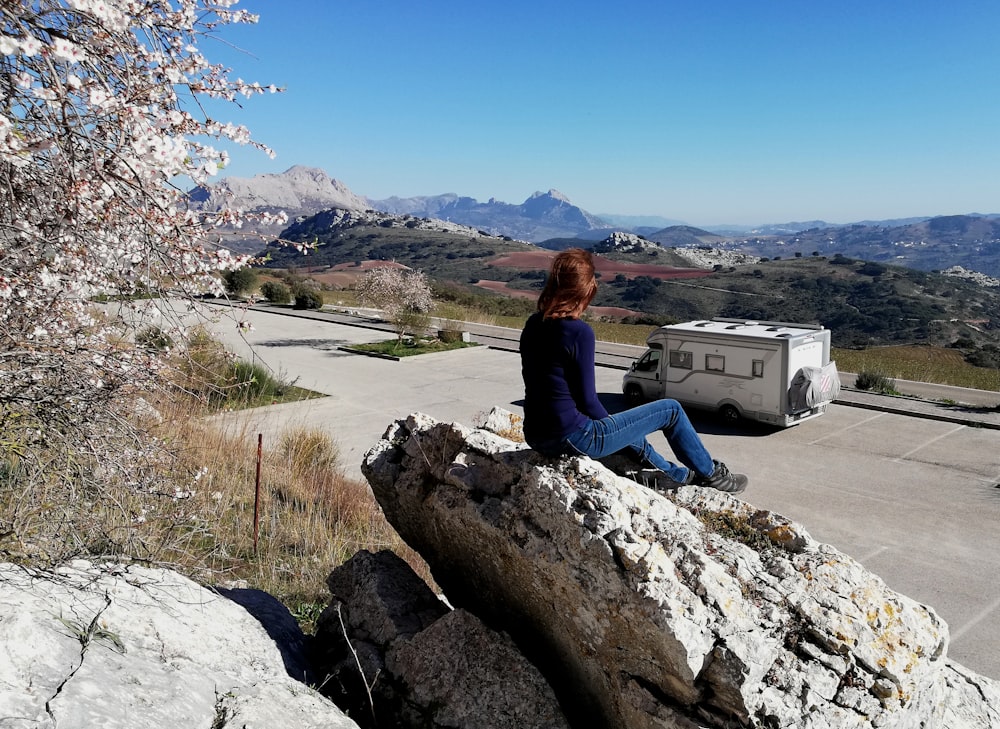 woman in black long sleeve shirt sitting on rock near body of water during daytime