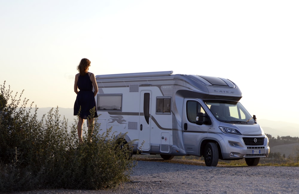 woman in black dress standing beside white and blue rv trailer during daytime