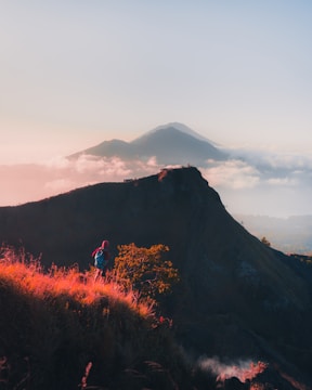Sunset over a mountain trail with a lone hiker enjoying the view.