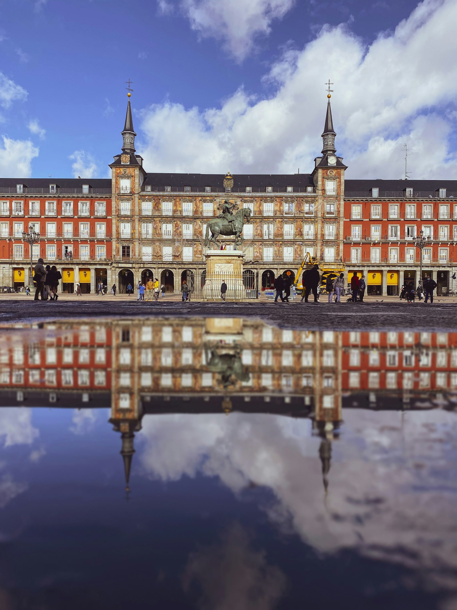 Plaza Mayor in Madrid, Spain, with its reflection visible in a rain puddle in the foreground