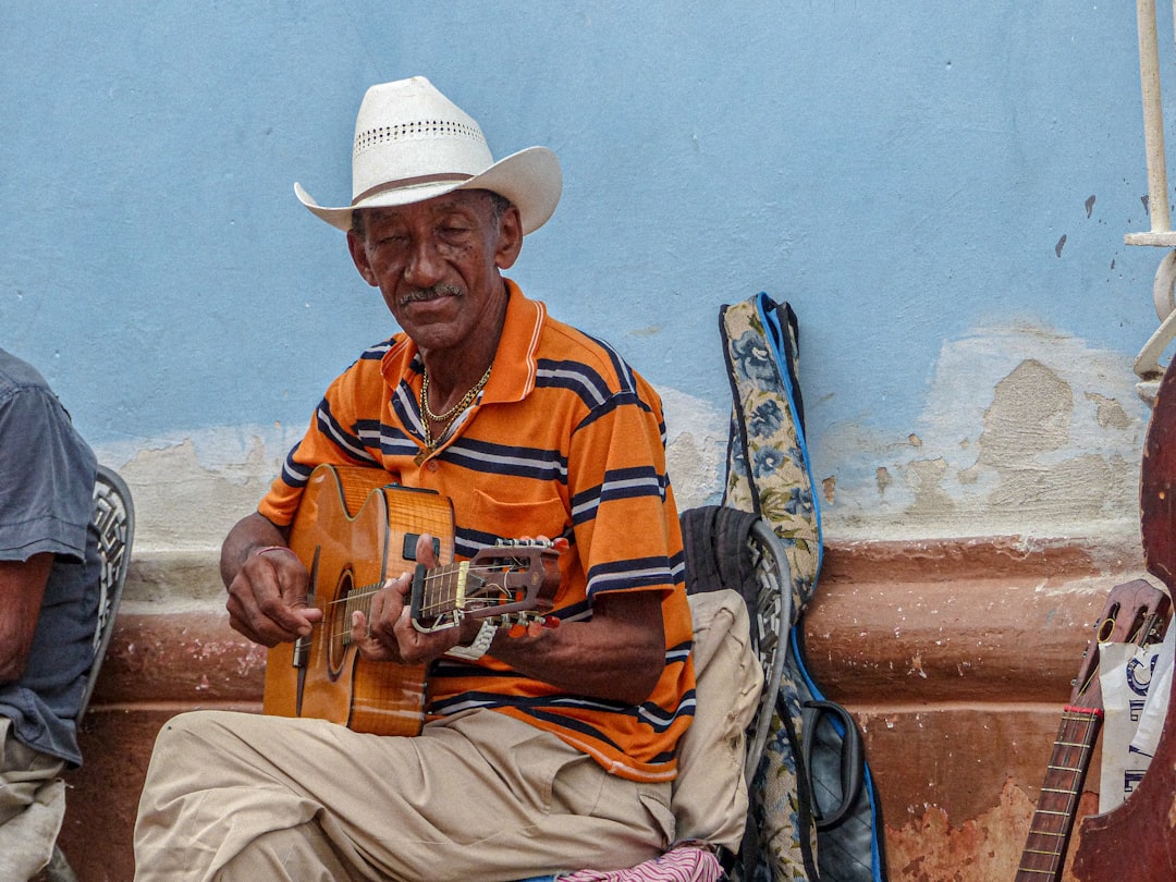 a man sitting on a bench playing a guitar, Musicien cubain