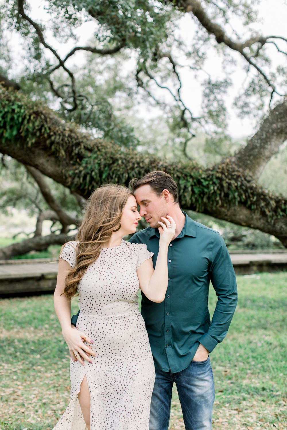 man in blue suit jacket kissing woman in white and black dress near tree during daytime