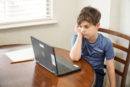 boy in blue crew neck t-shirt using macbook pro on brown wooden table